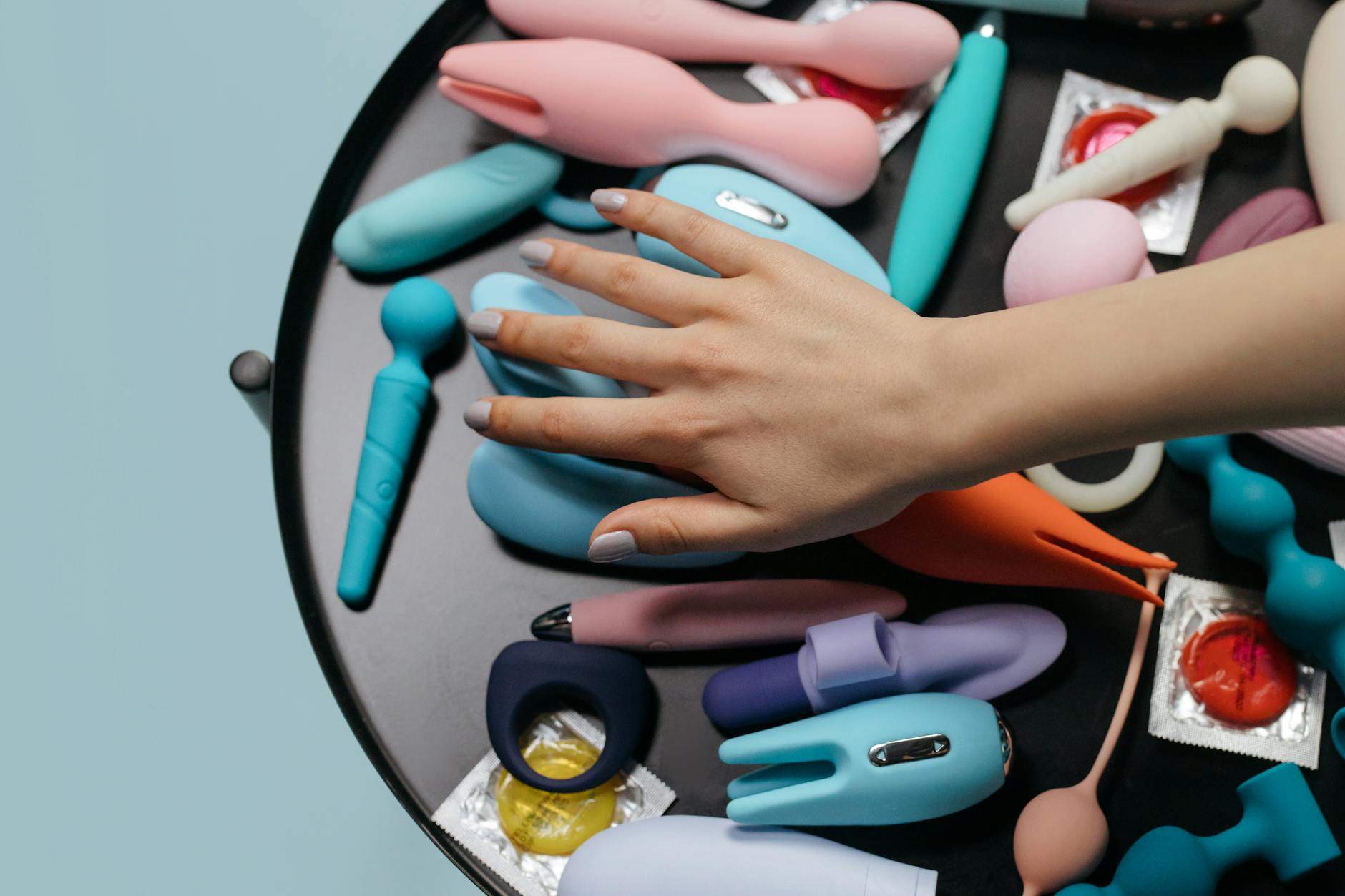 Two hands holding different-colored vibrators together on a neutral surface