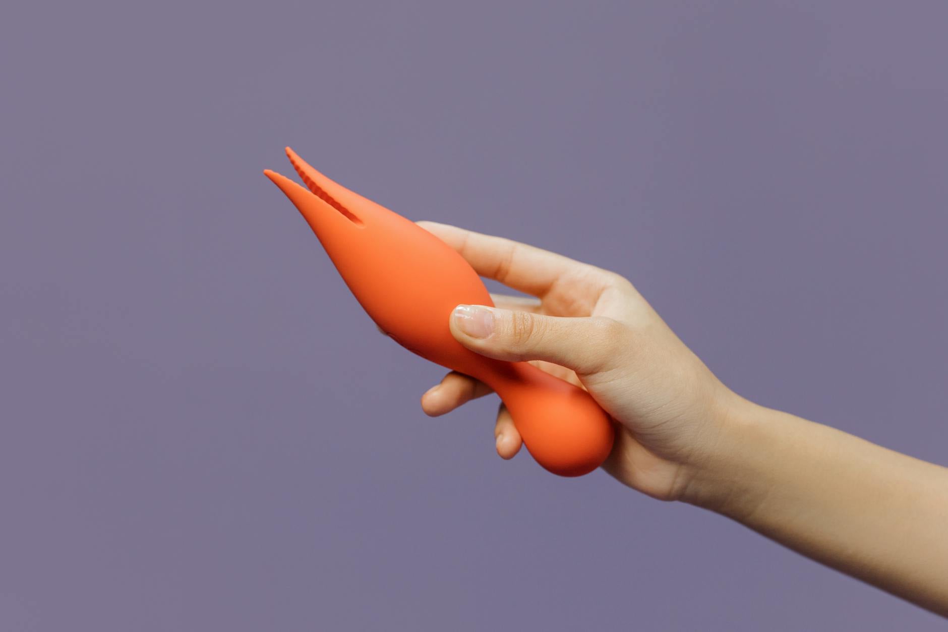 A close-up of a hand holding a vibrator against a minimalistic purple backdrop, showcasing modern sensuality.
