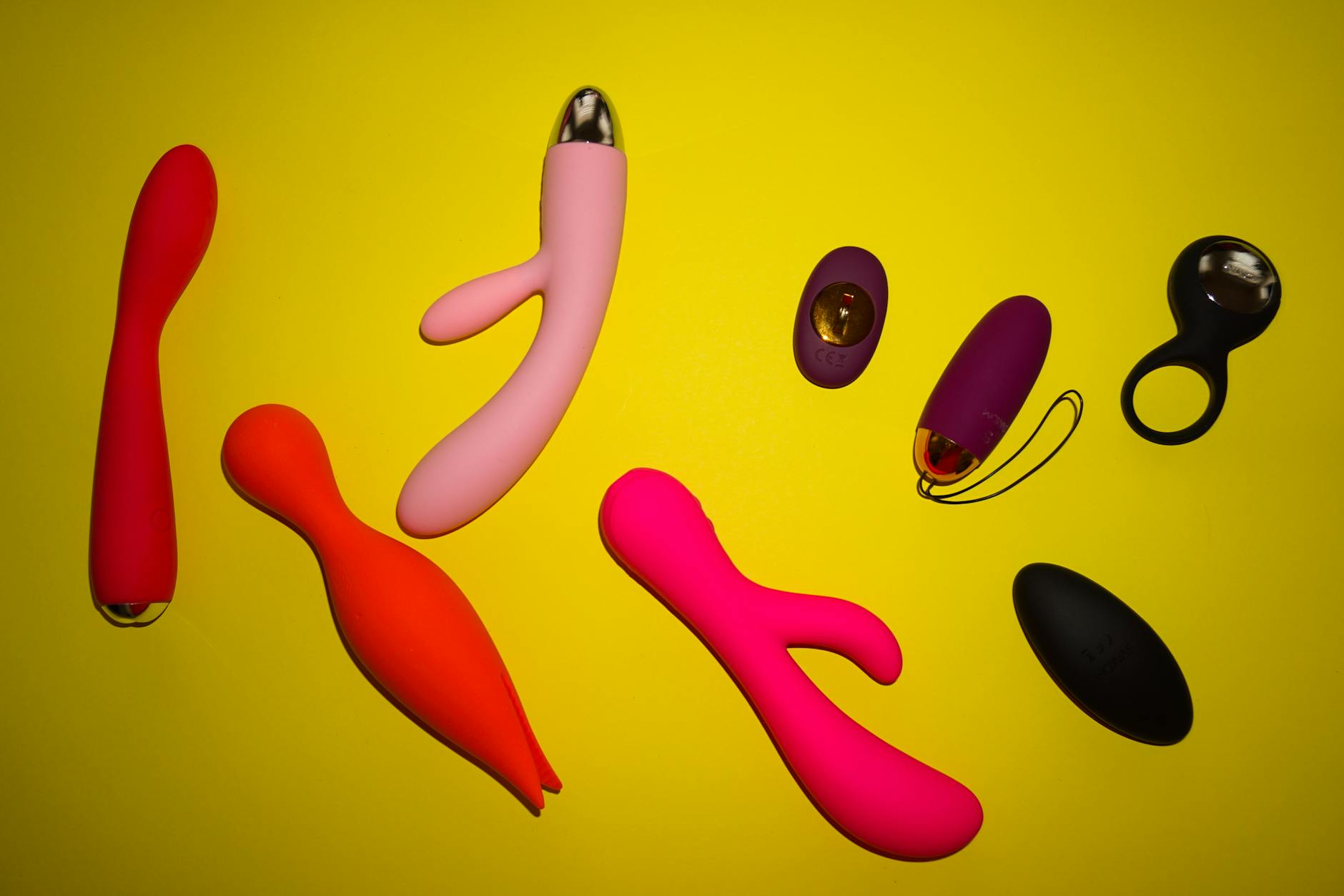 Vibrant arrangement of various colorful sex toys displayed on a bright yellow surface