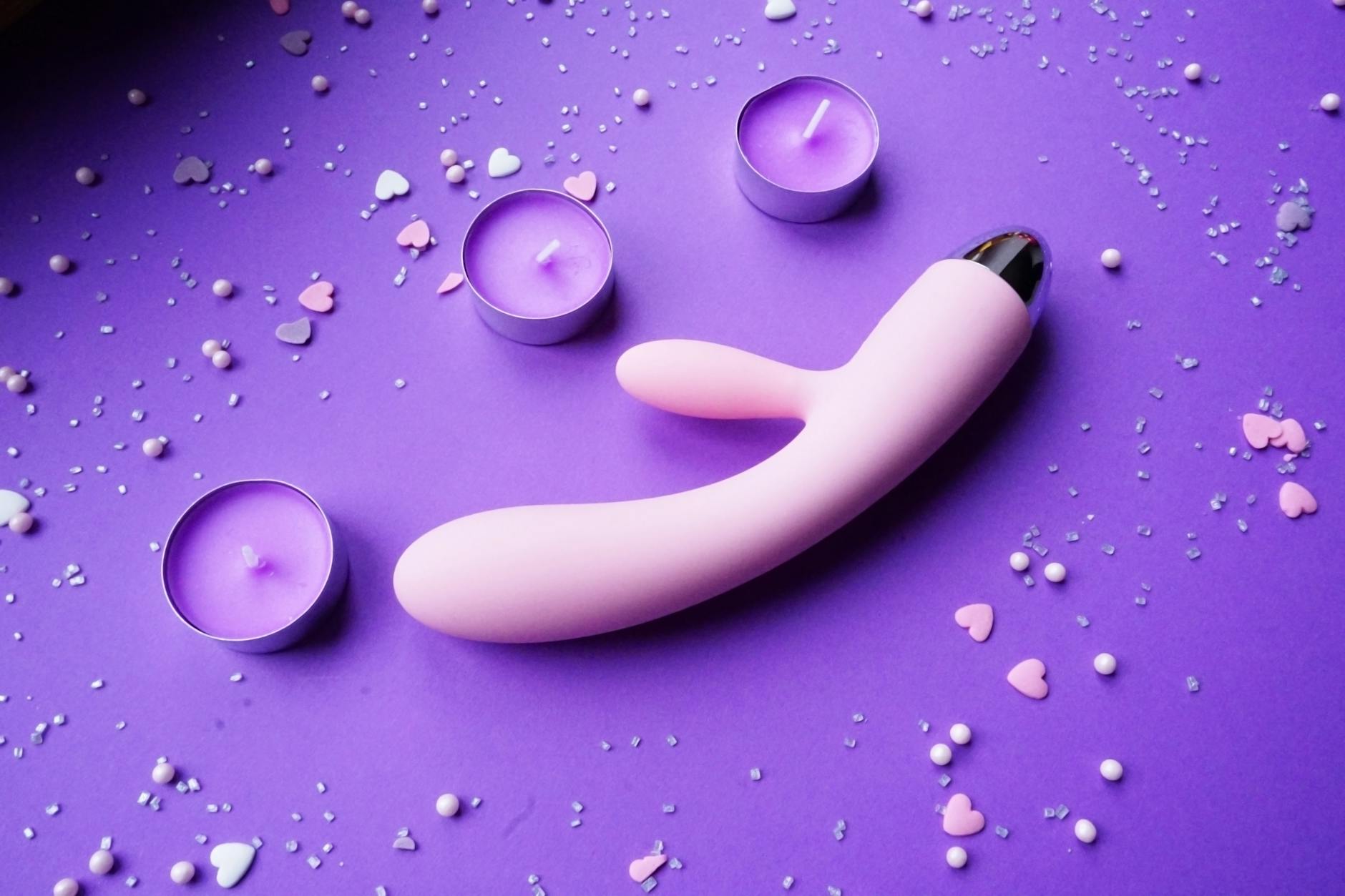 A blue silicone clitoral vibrator held in hand against a purple background, representing modern pleasure technology
